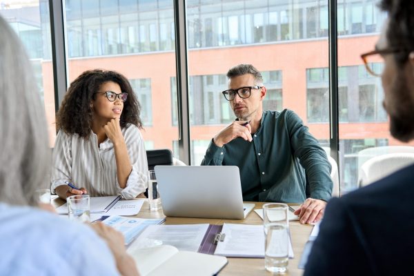 Male mentor leader manager talking to colleagues executive team, diverse partners group at executive board room meeting. Multicultural professional business people discussing project plan in office.